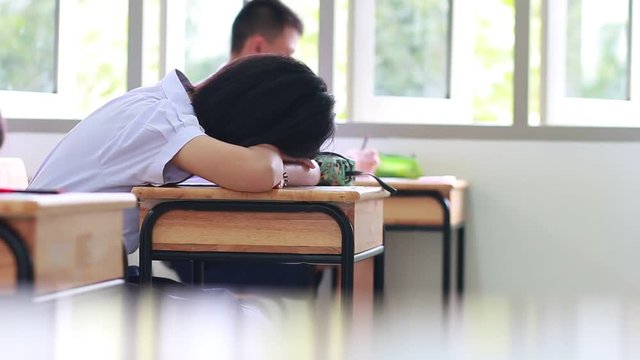 Behind Asian girl students in uniform sleeping in examination in classroom, educational school, view of having exams in class on seat rows, Education system tests of Thailand
