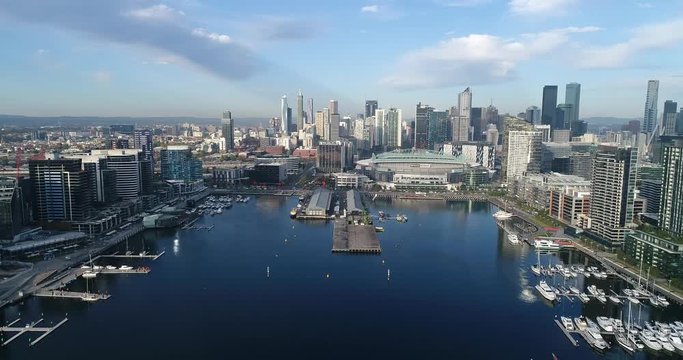 Aerial flying towards waterfront on Yarra river in Docklands suburb of Melbourne with view of city CBD towers.
