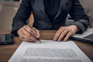 Close up businessman signing terms and agreement document on his desk in the office, business signing concept