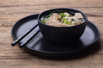 Japanese udon noodle soup with enoki  mushroom and tofu. The soup is served in a black ceramic bowl. Horizontal photo.