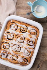 A white baking dish with fresh homemade cinnamon buns drizzled with cream cheese glaze. 
