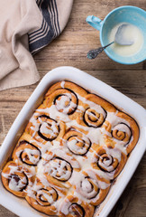 Cinnamon bun is a white baking dish. A blue cup with frosting next to the buns. 