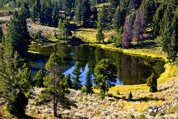 Fototapeta na wymiar A small, calm mountain lake reflecting its surroundings' beautiful fall colors