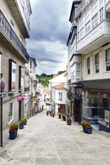 Betanzos, Galicia, Spain. July 30th, 2017: Commercial street with the floor of stone slabs and decorated with flower pots. Sky with clouds threatening rain and without people