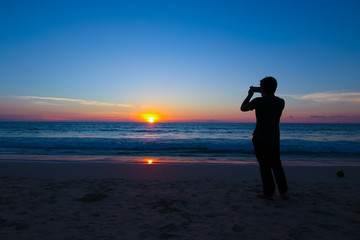 silhouette man on the beach taking the photo with his mobile during sunset at Phuket Thailand
