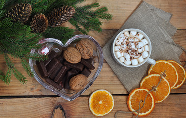 Coffee with marshmallow, bumps, nuts, chocolate and branches of a Christmas tree on a wooden table. View from above. Christmas and New Year. Still life.