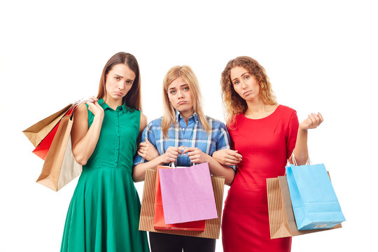 Portrait of three young girlfriends holding bunches of multi-colored shopping bags