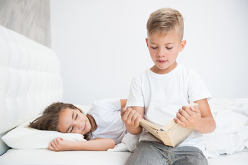 Brother reads a book to his sister  at bedtime