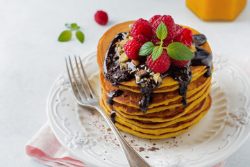 Pumpkin pancakes with fresh raspberries, chocolate and walnuts on  light stone or concrete background. Selective focus.