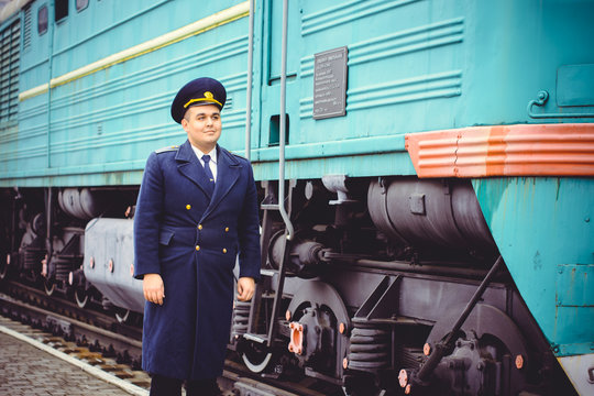 European or American train conductor is on his duty on a platform and other trains. Railway, steam trains, vintage trains