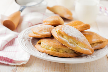 Pasties with cottage cheese and powdered sugar on a light wooden background. Traditional Russian pastry Sochnik. Selective focus. .