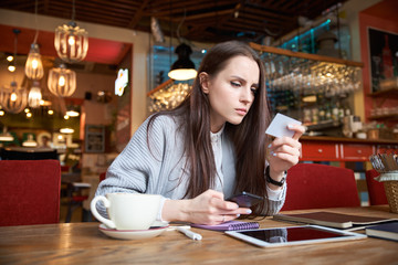 young successful attractive stylish woman makes payment by card Internet ordering sitting at a table in a cafe or bar