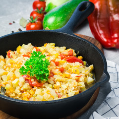 Summer squash tomato and paprika saute in cast iron skillet on concrete background. Vegan side dish. Selective focus, copy space. 