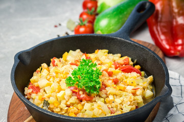 Vegetarian sauteed vegetables in cast iron skillet on concrete background. zucchini squash tomato carrot onion lentil. Selective focus, copy space. 