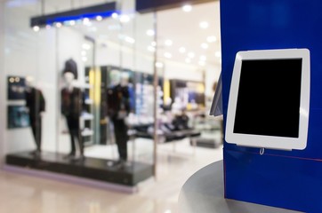 blank digital monitor or tablet on counter in front of men fashion clothes shop showcase in department store shopping mall, copy space for text or media content, marketing, advertisement concept