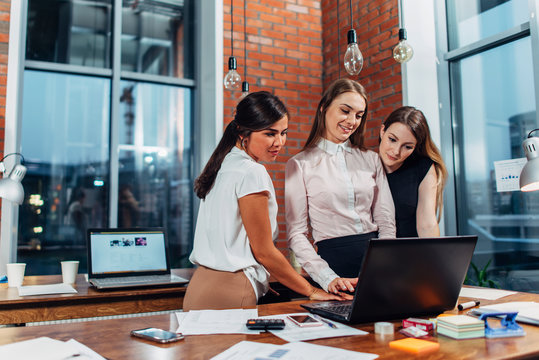 Woman showing the result of her work on laptop to colleagues standing in creative modern office