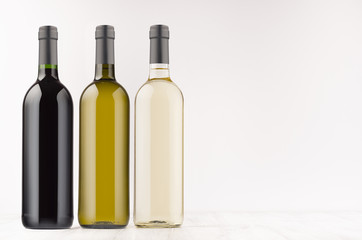 Wine bottles collection different colors - transparent, green, black- on white wooden board, mock up, copy space. Template for advertising, design, branding identity.