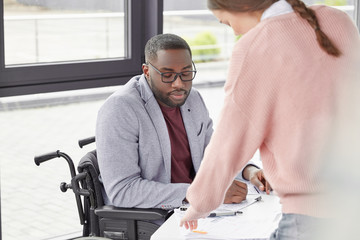 Serious dark skinned healthy challenged male dressed formally, comes in insurance policy to sign...