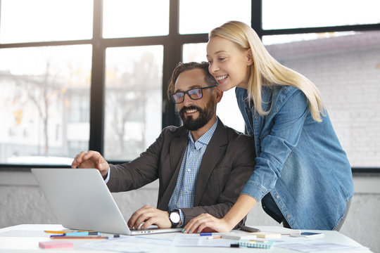 Portrait of successful active coworkers look at laptop computer, sit at work place in office, consult each other what information better to write. Professional investors work on future startup project