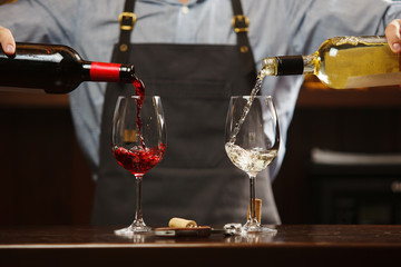 Male sommelier pouring red and white wine into long-stemmed wineglasses