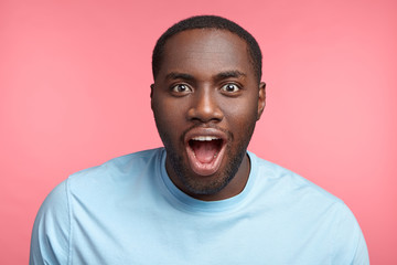 Emotional attractive Afro American male stares at presentation of new racing car, wants buy or try it, keeps jaw dropped and eyes widely opened, admires speed and comfort, has rapt attention