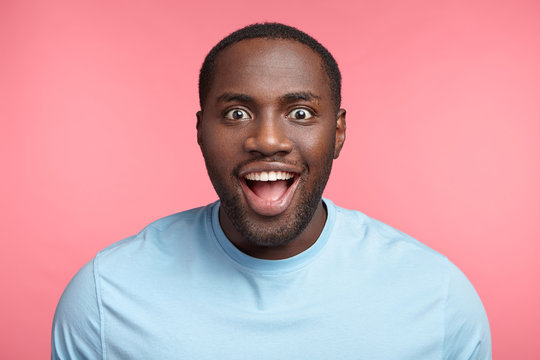 Portrait of excited dark skinned man stares at camera, sees what he likes greatly, has bated breath, wears casual clothes, isolated over pink background. Amazed black male model has stunned expression