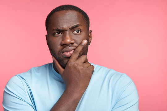 Portrait of serious dark skinned thoughtful male wears casual clothes, has pensive expression, isolated over pink background. Africam American plump man thinks about very importnat event in life