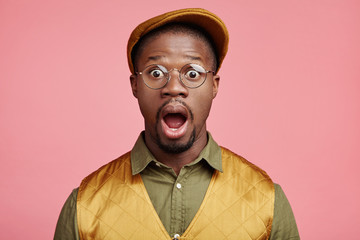 Horizontal portrait of amazed African male opens mouth widely, shocked about sales in web site, can`t believe in winning contest, wonders about latest news told by friend. Surprisment concept