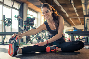 Smiling fit girl stretching legs in gym.