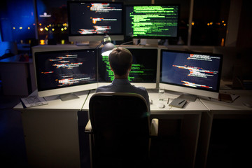 Rear view of hard-working programmer with stylish haircut sitting in front of computer and writing...