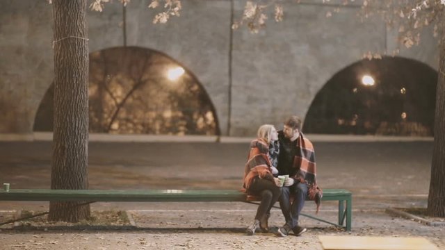 A young couple hug and kiss each other in a city Park at autumn cold night 