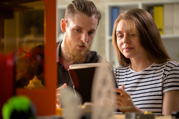 Talented young designers in casualwear using digital tablet while brainstorming on joint project concerning 3D printing, interior of modern lab on background