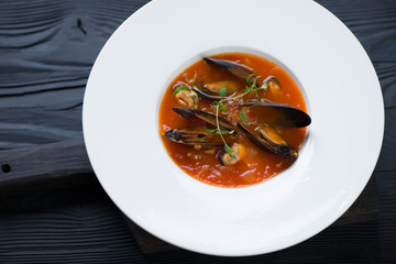 Tomato soup with mussels served in a white plate over black wooden background, horizontal shot