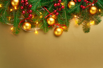 Christmas background decoration with lights, gold balls, berries and fir tree branches isolated on gold. Top view with blank space.