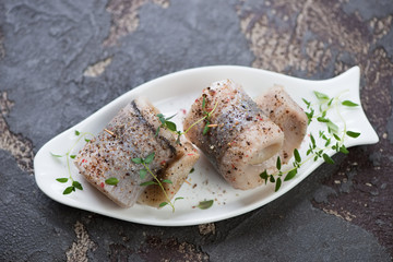 Fish-shaped plate with herring fillet rolls on a brown stone background, studio shot