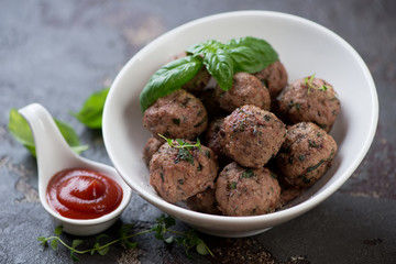 White bowl with freshly baked meatballs and sauce on a brown stone background, selective focus