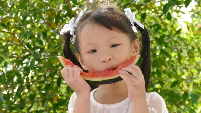 Portrait of little asian girl eating watermelon slices in park
