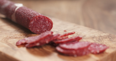 closeup female slicing thin salami sausage