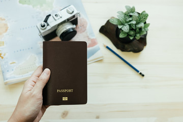 hand of women hold passport has retro camera, world map, pencil, plants placed on wooden table are background. image for equipment, travel, object, gedget, lifestyle, body concept