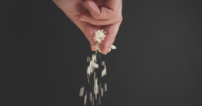 Closeup Of Man Hand Sprinkle Grated Aged Parmesan Over Dark Background