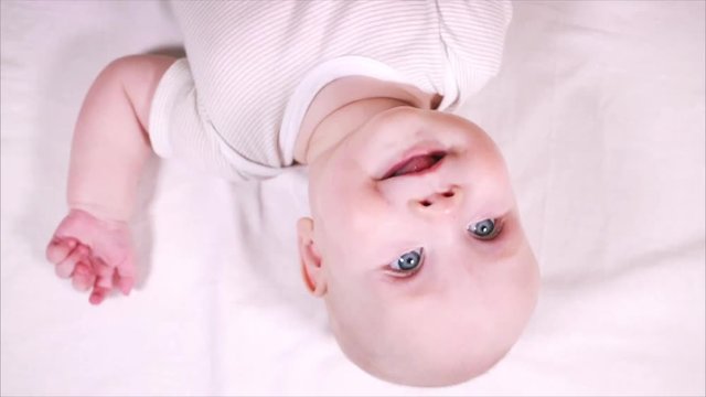 toothless child looking at the camera on a white background. A cute little baby is looking into the camera and is happy on a white bed sheet.