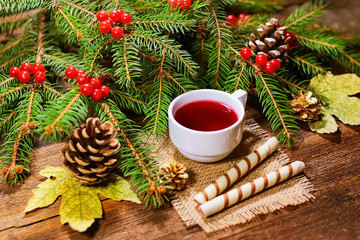 Obraz na płótnie Canvas rowan tea in a white cup on burlap and biscuits - straws. fir branches with rowan on a wooden board. Christmas theme.
