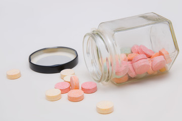 Colorful antacid tablets spilling out of glass bottle isolated on white