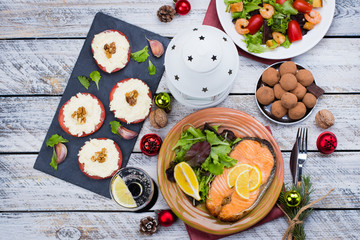 Christmas or New Year Family Dinner Setting Table Concept with Holiday Decoration. Delicious Roast Steak Salmon, Salade, Appetizers and Dessert on white wooden Background. Top view