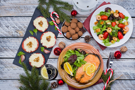 Christmas or New Year Family Dinner Setting Table Concept with Holiday Decoration. Delicious Roast Steak Salmon, Salade, Appetizers and Dessert on white wooden Background. Top view