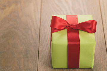 green paper gift box with red ribbon bow on oak table