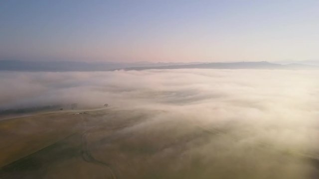 aerial view of misty cultivated hills at sunrise flying over