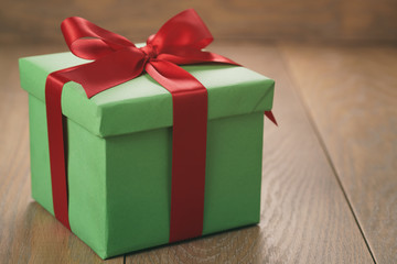 green paper gift box with red ribbon bow on oak table