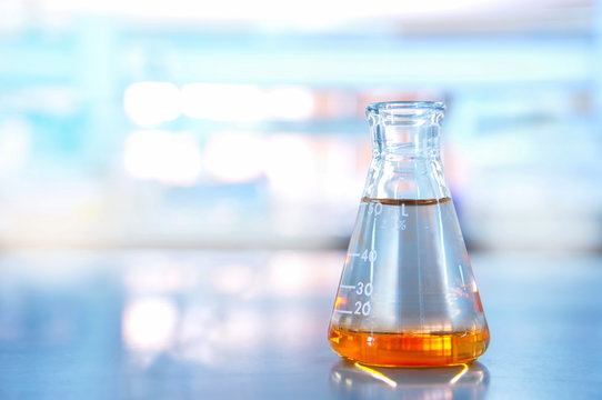 glass flask with orange solution in blue science laboratory background