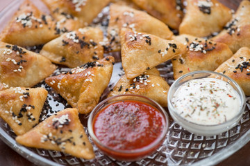Closeup of meat samosas topped with sesame and served with two sauces, selective focus